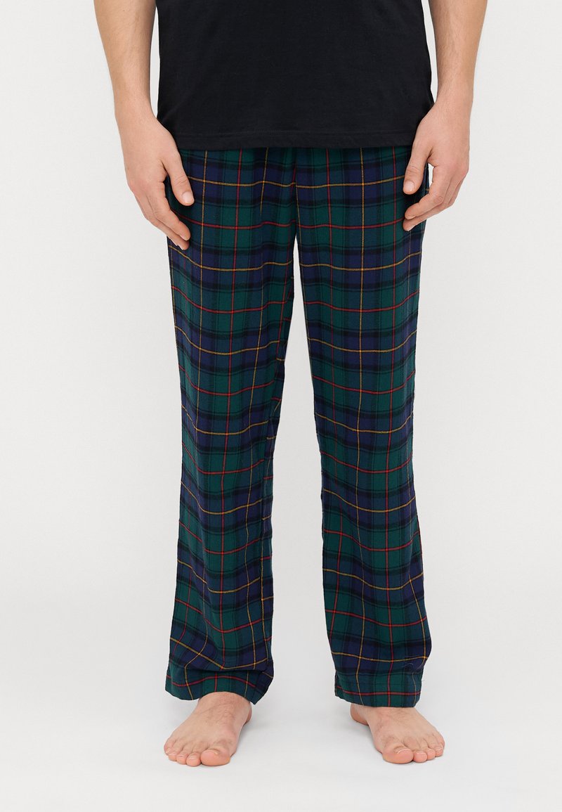 Pyjamas à carreaux verts avec des accents bleus et rouges, présentant une coupe ample et un tissu doux. Le pantalon tombe aux chevilles et n'a pas de fermetures visibles.