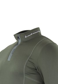 Pull-over vert foncé à manches longues avec demi-fermeture éclair et col montant. Fabriqué en matériau extensible, il présente des coutures plates et un logo sur le col.