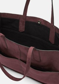 Bordowa torba typu tote zamszowa z czarną podszewką, wyposażona w dwa solidne uchwyty i zapięcie na zatrzask, wnętrze podzielone na kilka kieszeni.