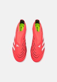Red synthetic soccer shoes with three white stripes, a slip-on design, ribbed texture, and a lightweight construction. Neon green inner sole.