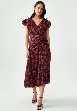 Black wrap dress with red floral pattern, featuring flutter sleeves, a tie at the waist, and a midi length. Paired with black strappy heels.