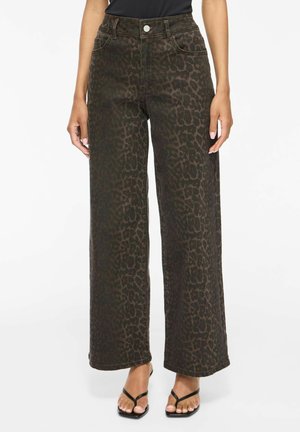 Weit geschnittene dunkelbraune Hose mit dezentem schwarzem Leopardenmuster, kombiniert mit schwarzen Riemchensandalen und einem schwarzen Oberteil.