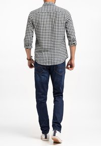 Czarna i biała koszula w kratę z podwiniętymi rękawami, w zestawie z niebieskimi dżinsami. Koszula ma klasyczny kołnierz i zaokrąglony dół.