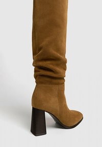 Botte mi-mollet en daim marron avec un bout arrondi, un design décontracté et un talon épais à texture bois foncé.