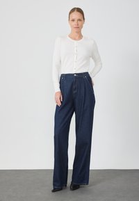 Lekki, biały kardigan z długim rękawem na guziki, połączony z ciemnoniebieskimi, szerokimi spodniami o wysokim stanie. Czarne buty na obcasie dopełniają stylizację.