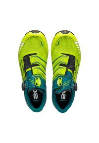 Lys gule atletiske sko med en mesh-overdel, teal accenter og et sikkert drejesystem til lukning. Har en struktureret sål for greb.
