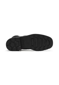 Suela de goma negra de un zapato Clarks con patrones de tracción profundos, mostrada desde abajo sobre un fondo blanco.