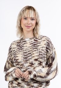 Megzta megztinis su tekstūruotu, daugiaspalviu raštu rudos, kreminės ir baltos spalvų. Turi apvalų apykaklę ir laisvą siluetą, su ilgomis rankovėmis.