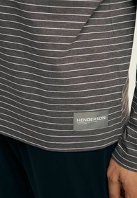 Graues Langarmshirt mit weißen horizontalen Streifen, aus weichem Stoff und mit gerundetem Saum. Verfügt über ein graues Etikett mit dem Text "HENDERSON".