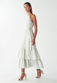 Juostelėmis dekoruota halter tipo suknelė su sluoksniuota skeltuke, turi juosmens juostą. Spalvos: šviesiai žalia ir balta. Sujungta su baltomis aukštakulnėmis šlepetėmis.