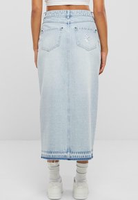 Jupe en denim bleu clair avec taille haute, poches arrière et détails à l'ourlet. Le tissu a une texture subtile avec un design long et droit.