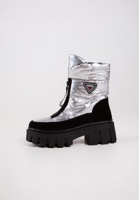 Bottines noires et argentées au design rembourré, avec un talon épais et un tissu texturé, ornées d'un patch en forme de triangle.
