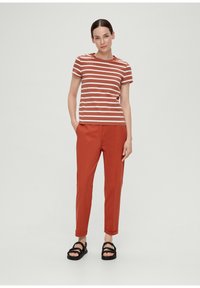 Gestreiftes T-Shirt in Rot und Weiß, kombiniert mit roten Hosen. Das Model trägt schwarze Sandalen. Einfacher, lässiger Schnitt mit kurzen Ärmeln.