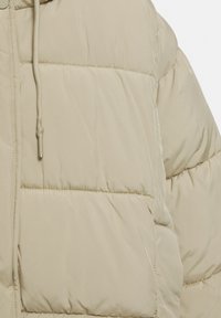 Giacca a vento in beige chiaro con design trapuntato, texture liscia, cordoncino regolabile al collo e discreti dettagli di cucitura.