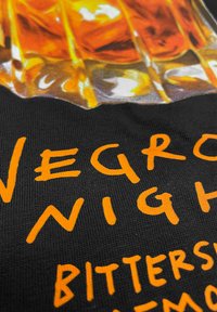 Black fabric with a glossy drink print featuring orange text reading "NEGRONI NIGHT" and "BITTERS." Text has a handwritten style.