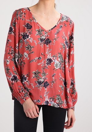 Rød blomsterbluse med V-udskæring, lange ærmer og elastiske manchetter; prydet med en blanding af mørkeblå og hvide blomsterprint mod et struktureret stof.
