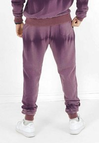 Lila Sweatpants mit elastischem Bund und Säumen, ausgestattet mit einer Gesäßtasche und einer strukturierten Oberfläche. Kombiniert mit weißen Turnschuhen.