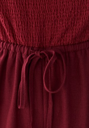 Raudona, tekstūruota medžiaga su surinkta elastine juosta ir raišteliu. Lygus paviršius su šiek tiek blizgesio. Tinka kasdieniam dėvėjimui.