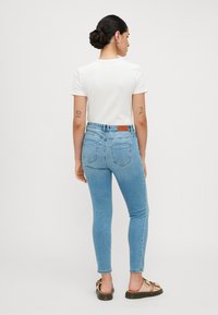 Lichtblauwe skinny jeans met een hoge taille en achterzakken, gecombineerd met een witte T-shirt met korte mouwen, bekeken vanuit de achterkant.