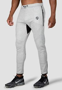 Grå atletiske joggere har et tætsiddende design med sorte sidepaneler, lynlås lommer og en justerbar taljebånd med snore.