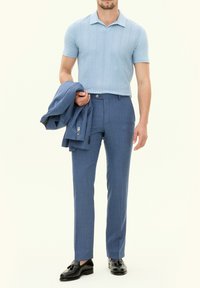 Polo en tricot bleu clair à manches courtes, associé à un pantalon bleu sur mesure et un blazer assorti, complété par des chaussures noires.