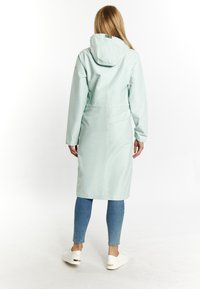 Light mint green waterproof coat with a hood, cinched waist, long sleeves, and a mid-length design, paired with blue jeans and white sneakers.