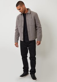 Szary żakiet z wełny z kołnierzem, dwoma kieszeniami na piersi i zapięciem na guziki, zestawiony z czarnym swetrem i czarnymi dżinsami.