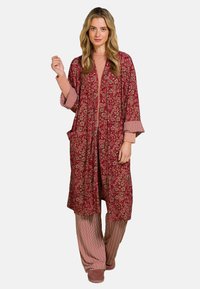 Lange rode kimono-achtige nachtjapon met bloemmotief, open voorkant en brede mouwen. Gecombineerd met gestreepte wijde broek en roze slippers.