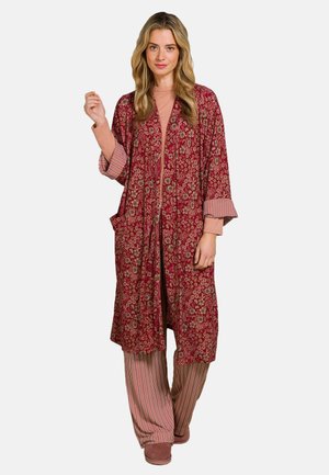 Lange rode kimono-achtige nachtjapon met bloemmotief, open voorkant en brede mouwen. Gecombineerd met gestreepte wijde broek en roze slippers.