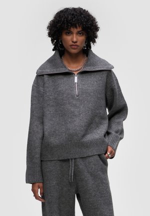 Gray knitted sweater with a high collar, half-zip front, and ribbed cuffs and hem. Soft texture paired with matching gray bottoms.