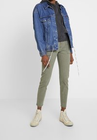 Blå denimjacka med elastiska muddar, grå hoodie under, olivgröna tapered byxor och beige högstövelsneakers.