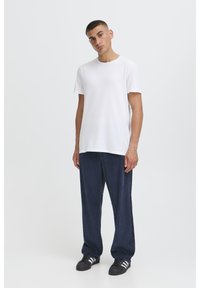 Bílé bavlněné tričko spojené s tmavě modrými manšestrovými kalhotami. Oblečení má volný střih a jednoduchý design, doplněný o černé tenisky.