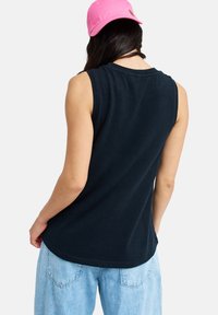 Αμάνικη μπλε ναυτική μπλούζα με στρογγυλή λαιμόκοψη, ομαλή υφή και άνετη εφαρμογή. Συνδυασμένη με ανοιχτόχρωμα φαρδιά τζιν.