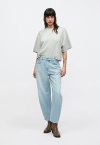 Γκρι κοντομάνικο, φαρδύ τοπ σε oversized στυλ, συνδυασμένο με ανοιχτό μπλε τζιν παντελόνια με φαρδιά πόδια. Τα ταμπα μποτάκια στον αστράγαλο ολοκληρώνουν την εμφάνιση. Απλός, καθημερινός σχεδιασμός.