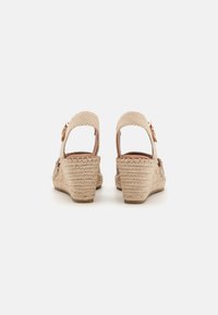 Sandali con zeppa e tomaia intrecciata beige, tacco aperto, cinturino alla caviglia regolabile e suola testurizzata per una buona presa. Presenta una fibbia decorativa.