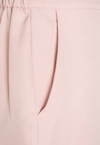 Tecido rosa claro com pregas e um bolso lateral. Textura suave e superfície lisa, projetado para conforto e facilidade de uso.
