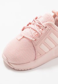 Rosa träningsskor med mesh- och textilöversida, med en texturerad design, snörning och tre distinkta vita ränder på sidan.