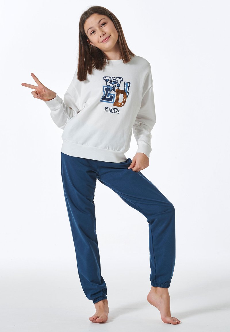 Weißes Sweatshirt mit blauem und braunem Grafikdruck, kombiniert mit blauen Jogginghosen, die Gummibündchen und eine lockere Passform bieten.