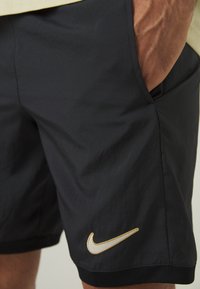 Shorts de sport noirs en matériau léger. Présentent un logo Nike doré au bas et une texture en maille à la taille.