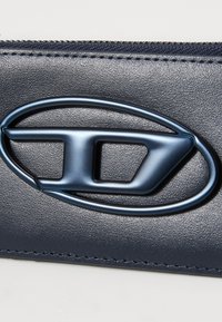 Navy blue leather wallet featuring a prominent oval logo in dark metallic, with a textured finish and contrasting stitching along the edges.