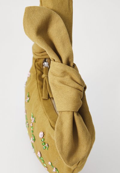 Kollane sinepikoti, mida kaunistavad roosad lillemotiivid ja rohelised aktsendid, on varustatud sõlmitud käepidemega, lukuga ja tekstuurse pinnaga.