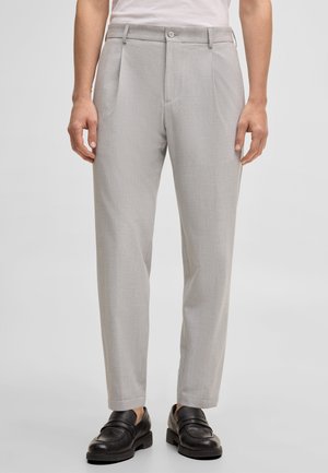 Hellgraue, gerade geschnittene Hose mit Falten, Seitentaschen und Knopfverschluss, getragen mit schwarzen Lederloafern und einem weißen, in die Hose gesteckten Hemd.