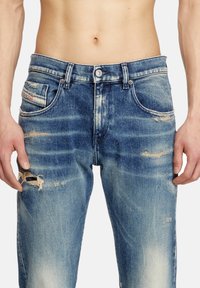 Jean en denim bleu clair avec des détails déchirés, y compris des patchs effilochés et un effet usé. Comprend une fermeture à bouton et un design à cinq poches.