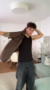 Smeđa košulja s dugim rukavima nosi se preko crnog topa bez rukava, uz tamne traperice. U pozadini se nalaze svijetlosmeđi namještaj u dnevnoj sobi.