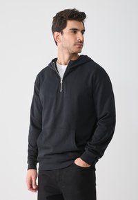 Sudadera con capucha negra hecha de una suave mezcla de algodón, que cuenta con media cremallera, bolsillo frontal y puños acanalados. Diseño sencillo sin patrones.