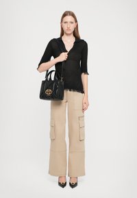 Black knit top with short sleeves; beige cargo pants with pockets; black quilted handbag with a gold logo; black pointed heels.