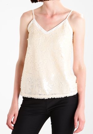 Beige paljettanktop med V-udskæring og tynde stropper. Stoffet er tekstureret med overlappende paljetter, parret med sorte skræddersyede bukser.
