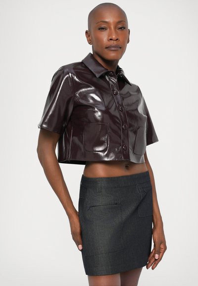 Rövid ujjú, fényes bordó anyagból készült cropped ing, gombos elülső résszel és két elülső zsebből, sötétszürke farmer szoknyával párosítva.