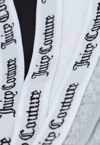 Biely textil s čiernym nápisom "Juicy Couture" v štýlovom písme, vyzdvihujúci hladkú textúru a opakujúci sa vzor.