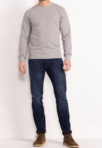 Sudadera gris con cuello redondo, mangas largas, puños y dobladillo de canalé. Combinada con vaqueros oscuros ajustados y botas marrones con cordones.